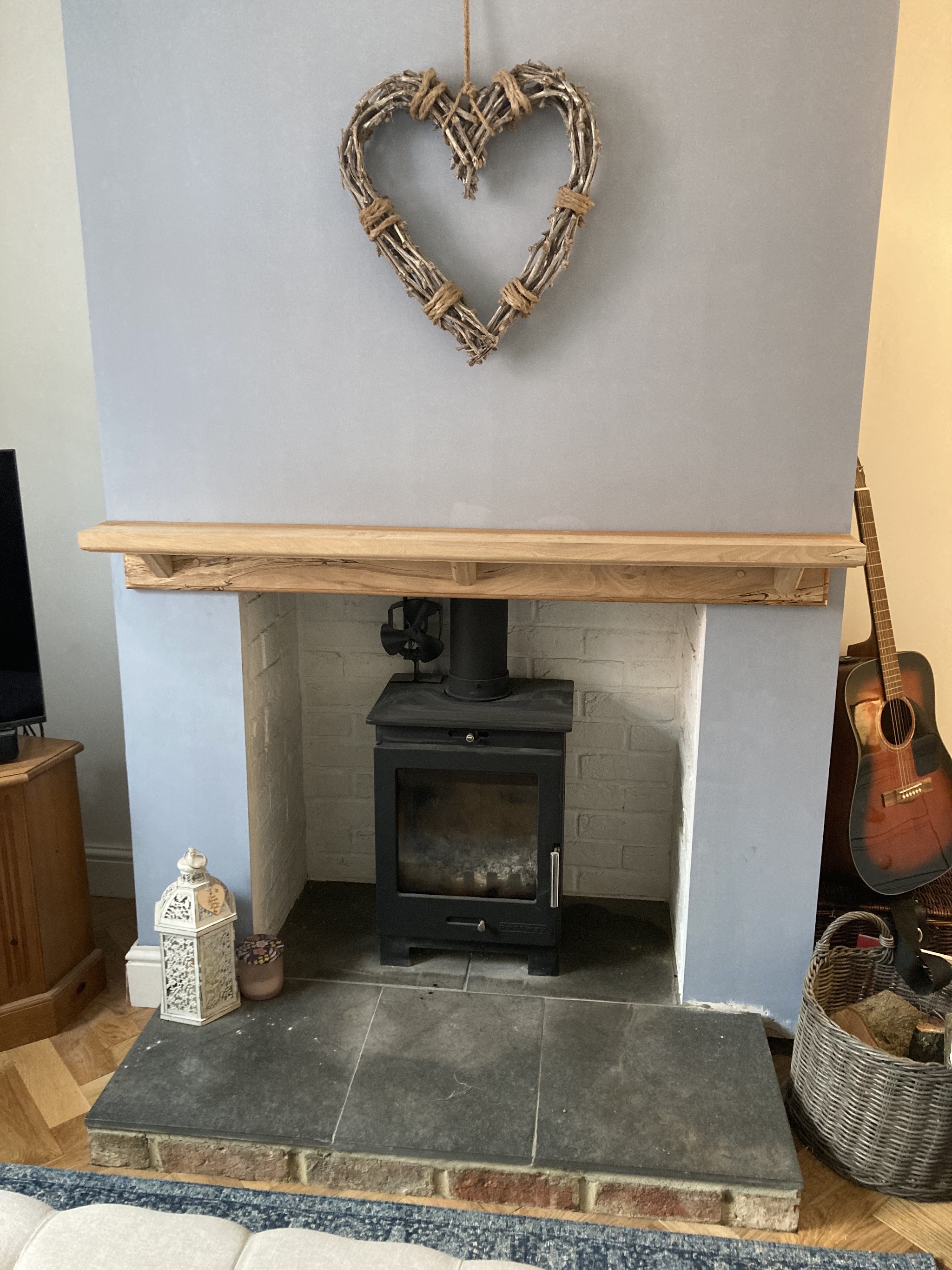 A black wood-burning stove in a whitewashed fireplace with a timber beam and slate hearth
